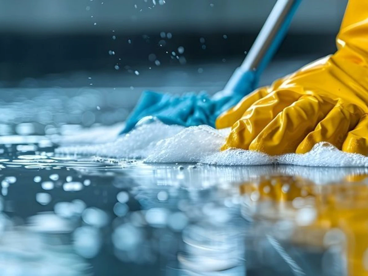 Gloved hands scrubbing a surface with foam and water spray